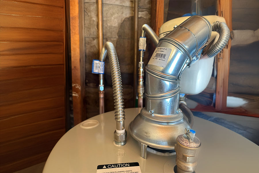 Close-up of water heater top with metal vent and flexible pipes