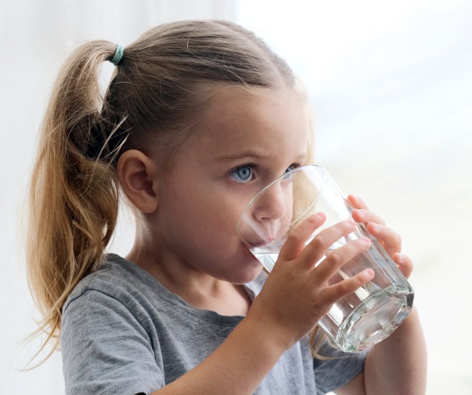 young girl drinking from large clear glass of water