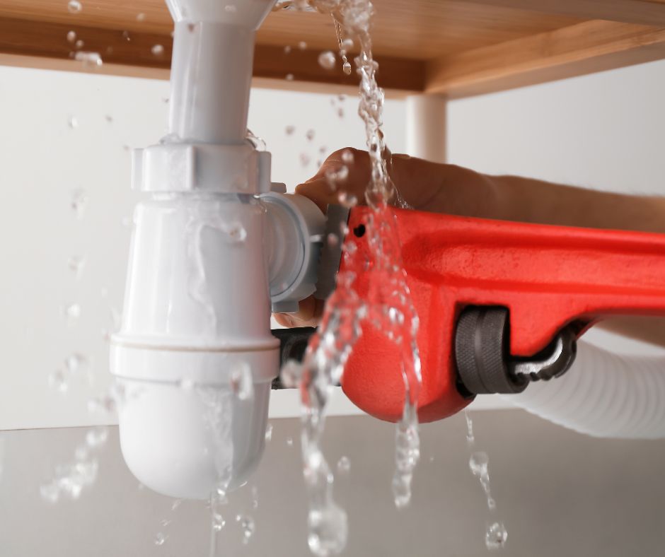 San Diego plumber using wrench under sink on pipe with water leak