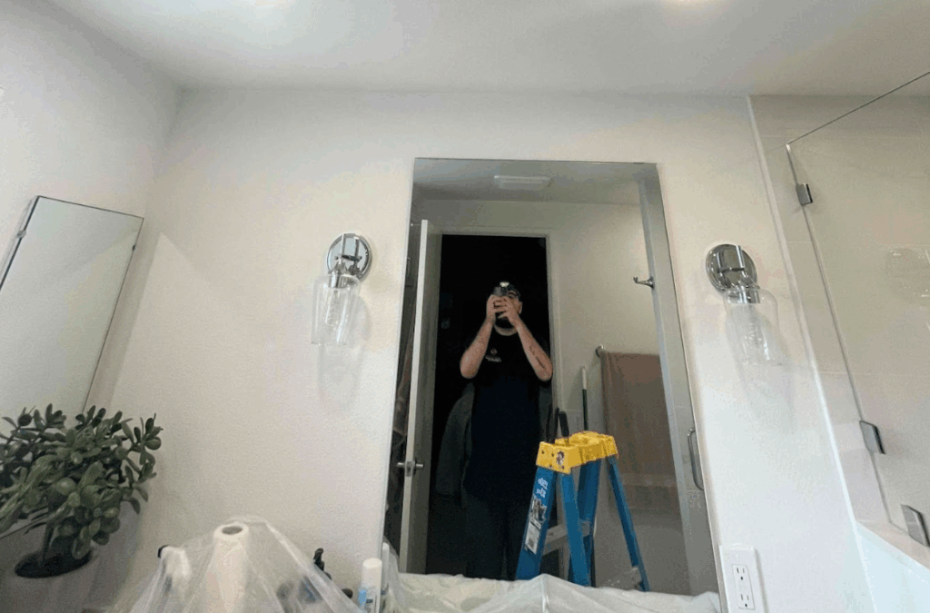 A bathroom interior with a technician visible in the mirror taking a photo.