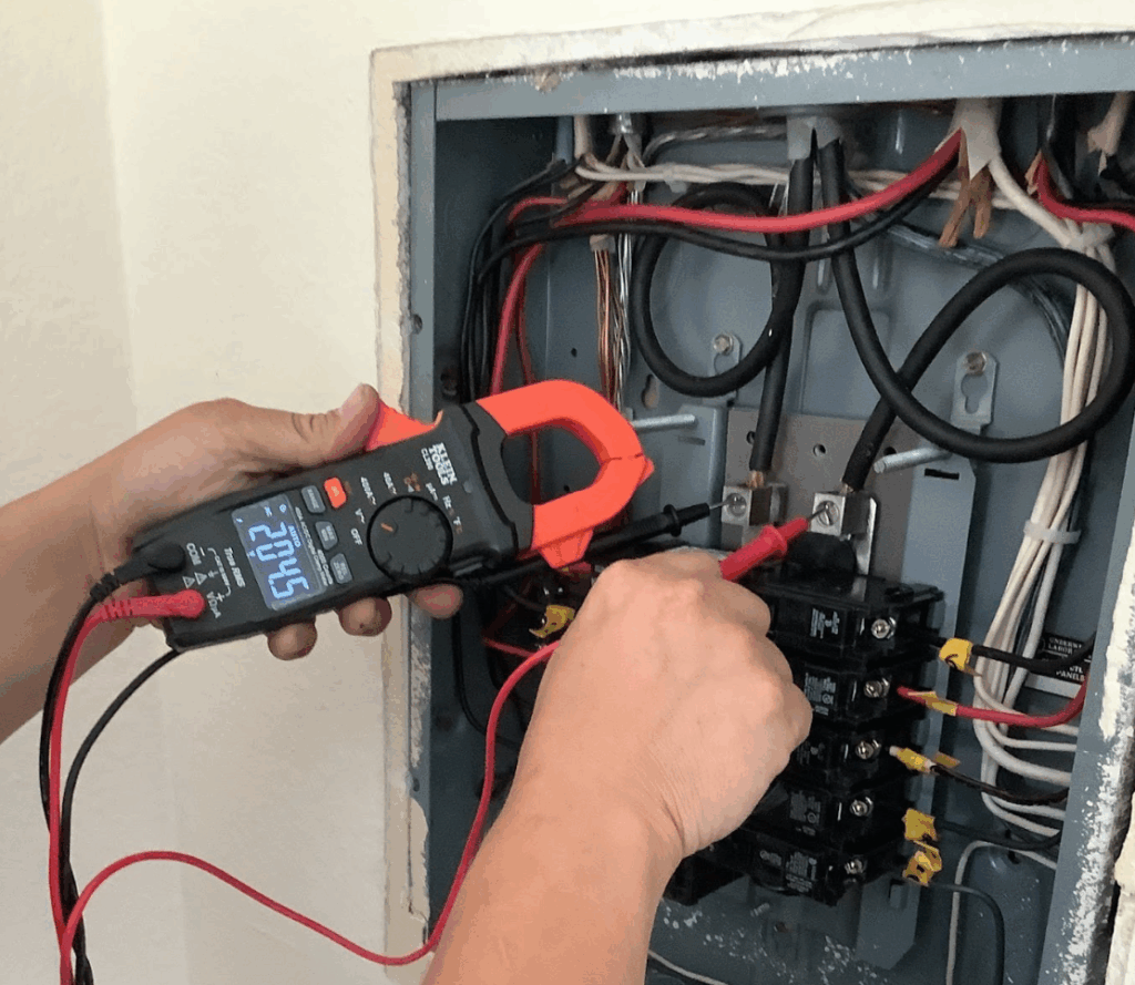 A close-up view of hands holding a meter and probes against an open electrical breaker panel.