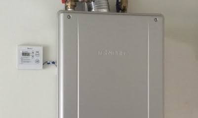 A tankless water heater mounted on a wall with a digital temperature controller beside it.