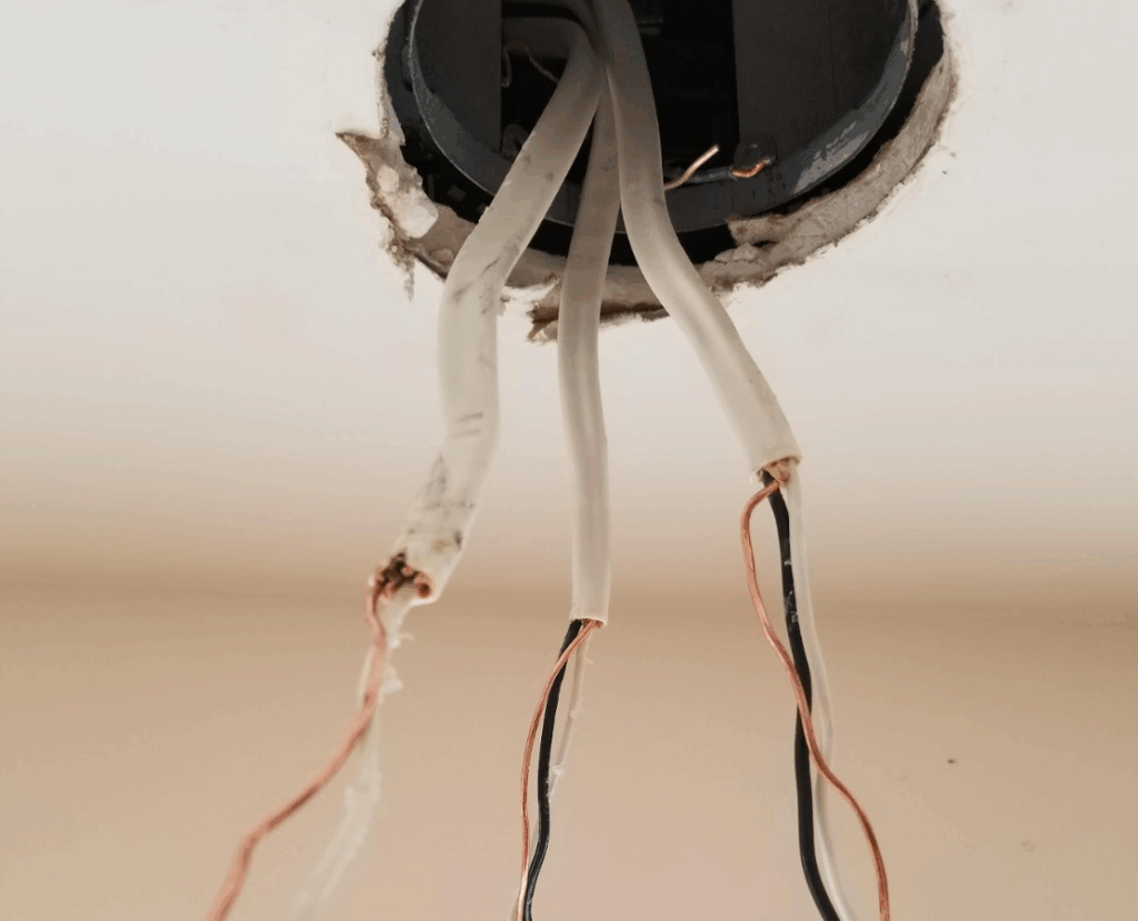 Close-up of ceiling electrical box with exposed copper wires.