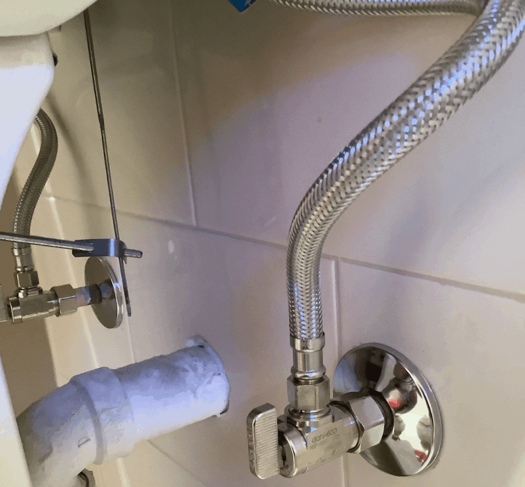 Close-up of stainless steel braided plumbing supply lines connected to a shut-off valve.