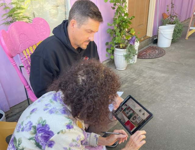 Electric technician reviewing service details on a tablet with a homeowner on an outdoor porch