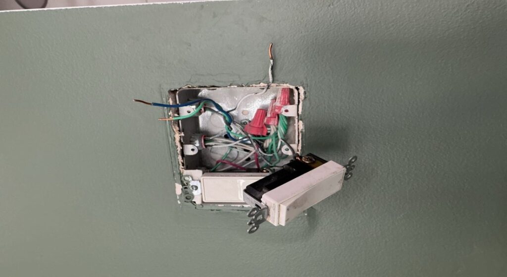 Open electrical junction box showing exposed wiring and a disconnected wall switch during replacement.