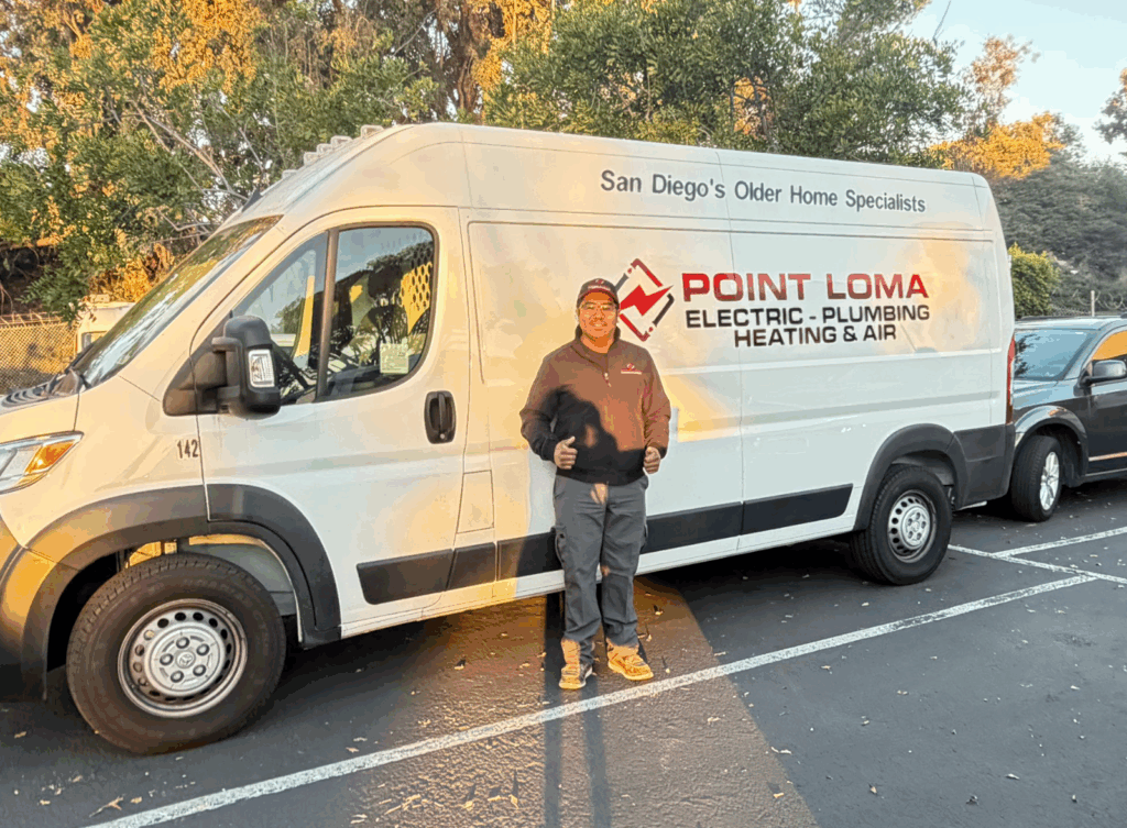Smiling electrician standing beside white Point Loma Home service van.