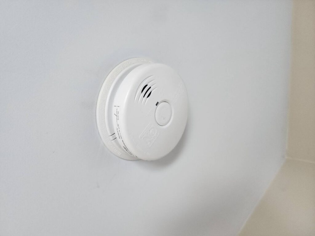 White circular smoke detector mounted on white ceiling.