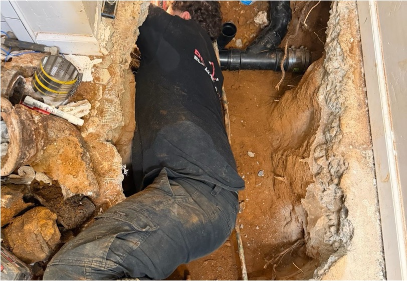 A plumber is getting dirty working on an underground pipe issue