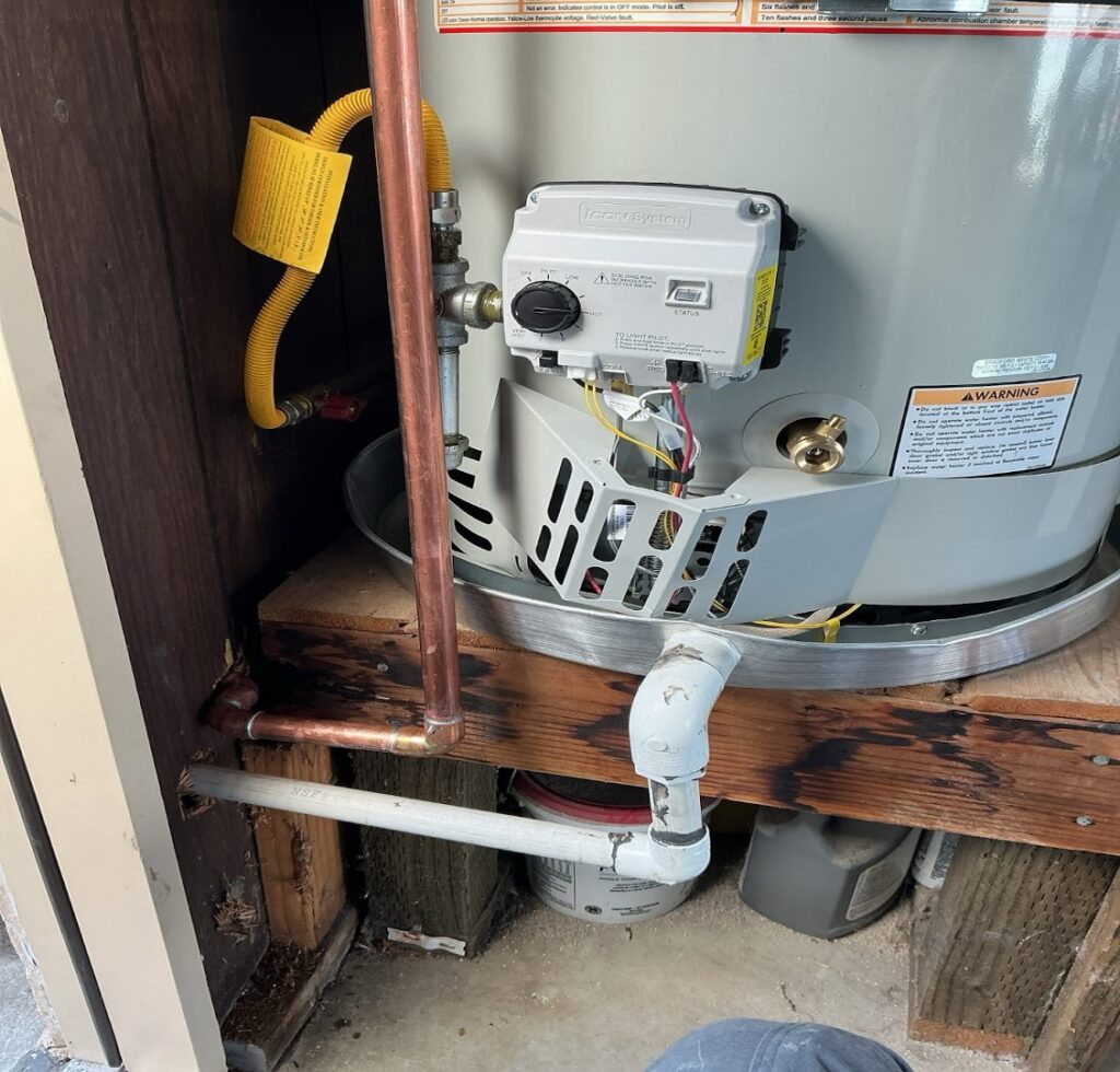 Close-up of a white, gas water heater with a control valve and copper piping.