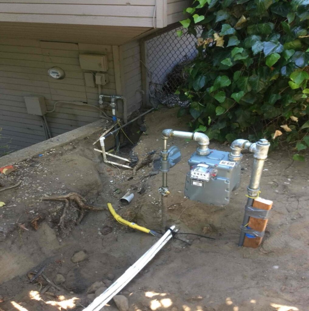 Gas meter and yellow gas line installation in an excavated area beside a home's foundation