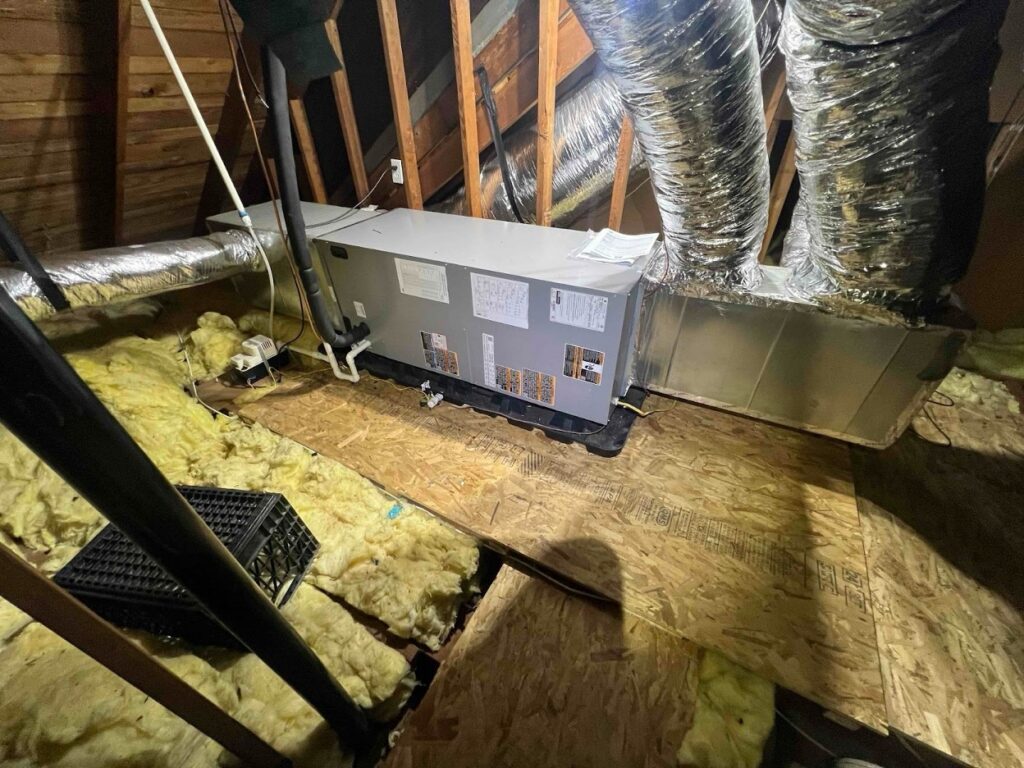 Newly installed air handler unit in an attic, surrounded by insulated ductwork and insulation
