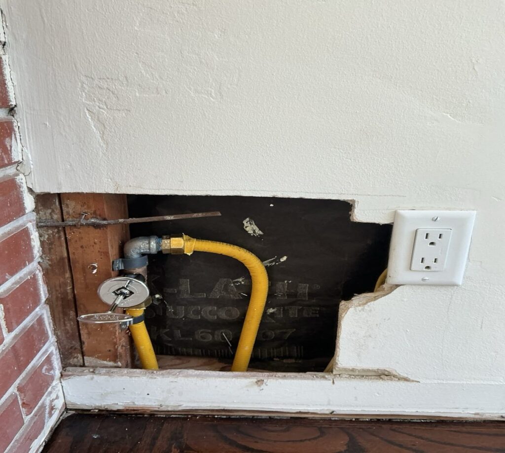 Yellow flexible gas line and shut-off valve installed through an opening in drywall