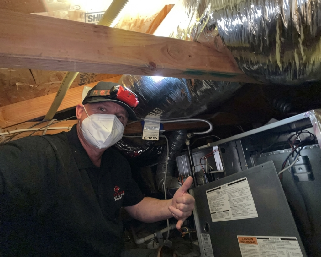A Point Loma Home Pros technician working on a furnace in a tight crawl space.