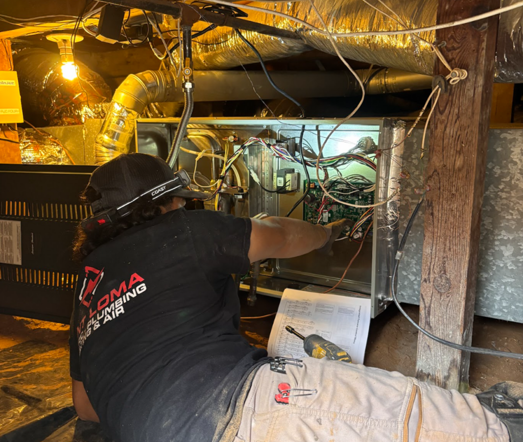 A Point Loma technician wearing a headlamp works on the control board wiring of a furnace