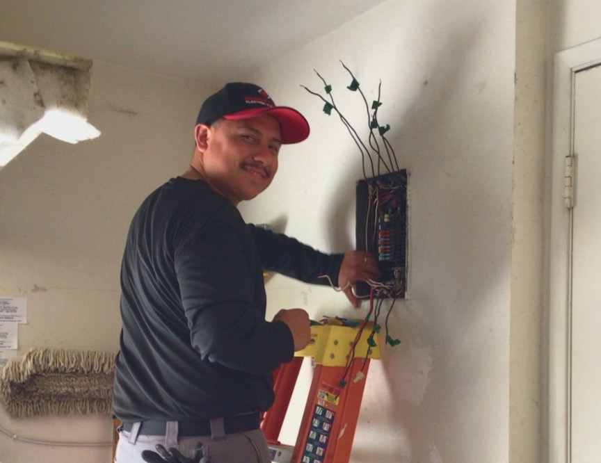 Point Loma Home Pros electrician on a ladder inspecting exposed wiring at a residential electrical panel
