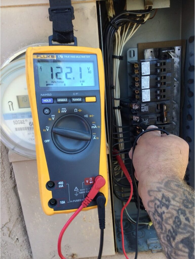 Point Loma Home Pros technician testing voltage at an outdoor electrical panel next to an SDG&E meter.