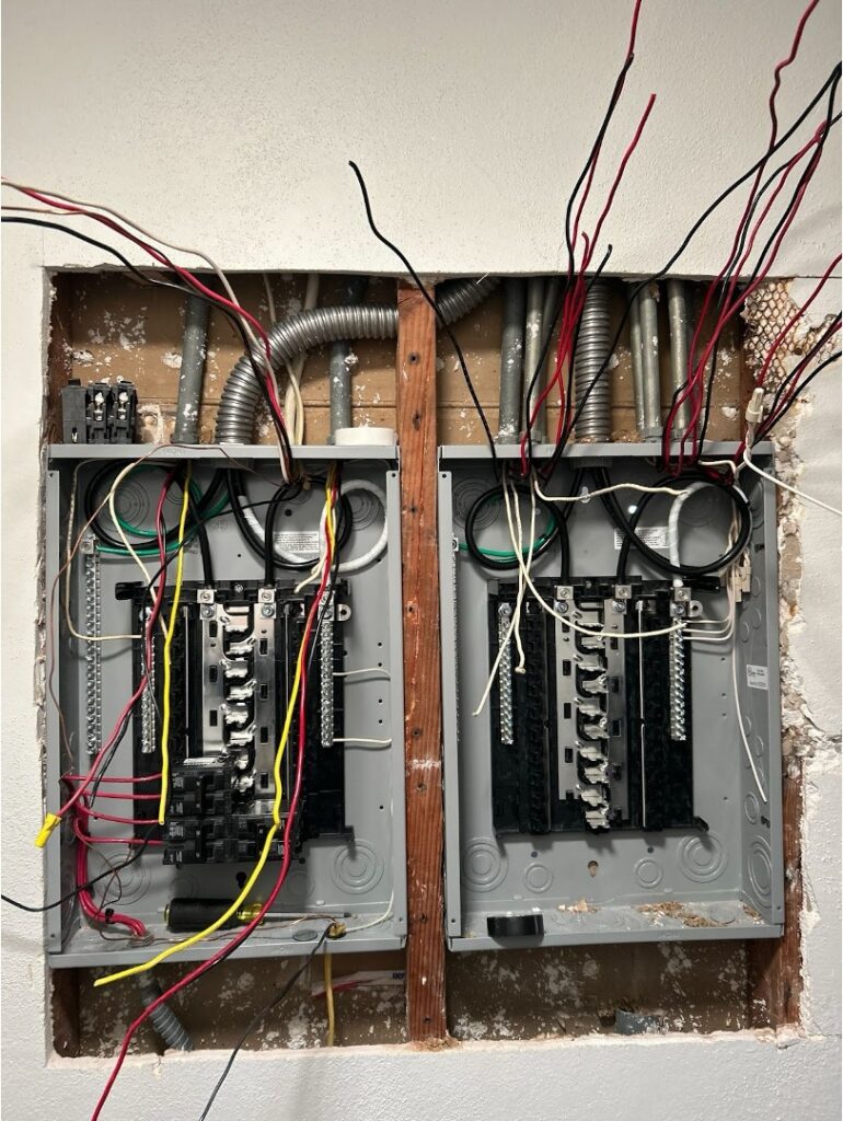 Two residential electrical panels with exposed wiring during a mid-installation panel replacement in a San Diego home.