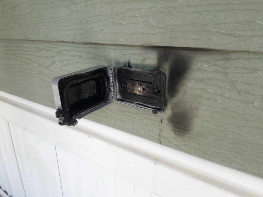 Burned and scorched outdoor GFCI outlet box showing visible fire damage from electrical arcing
