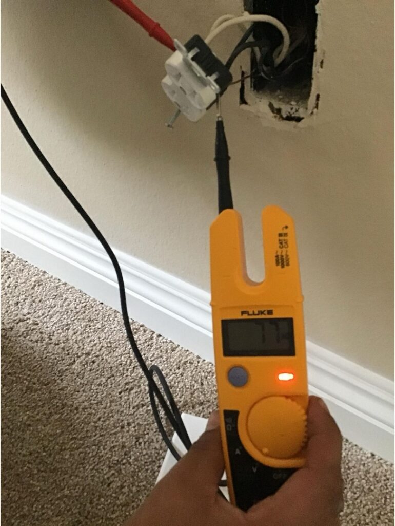 Electrician testing a residential wall outlet with a Fluke voltage tester during an inspection in a Clairemont home