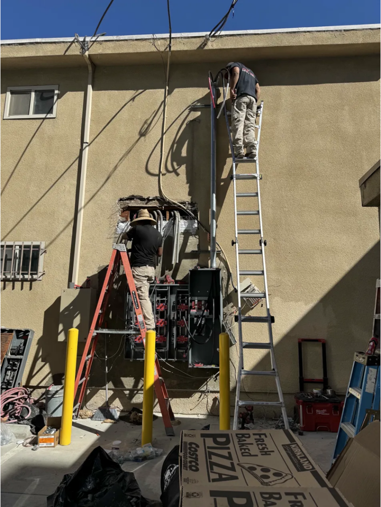 Two licensed electricians installing a new exterior electrical panel during a Del Mar home upgrade