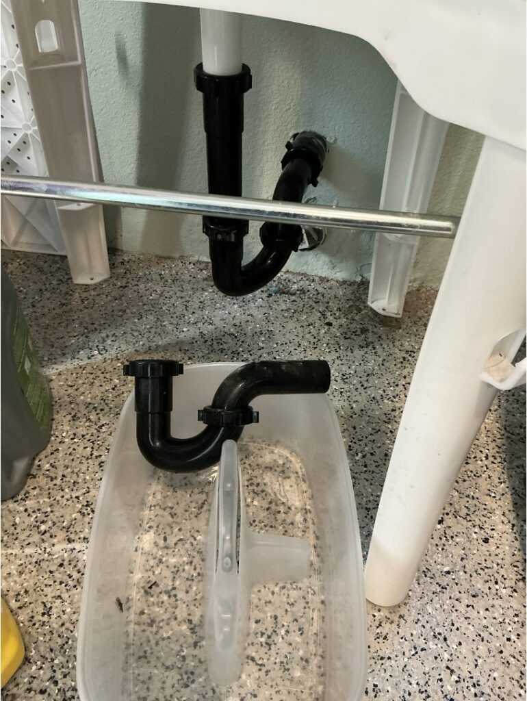 Under-sink plumbing with a black P-trap and drain lines in a San Diego home