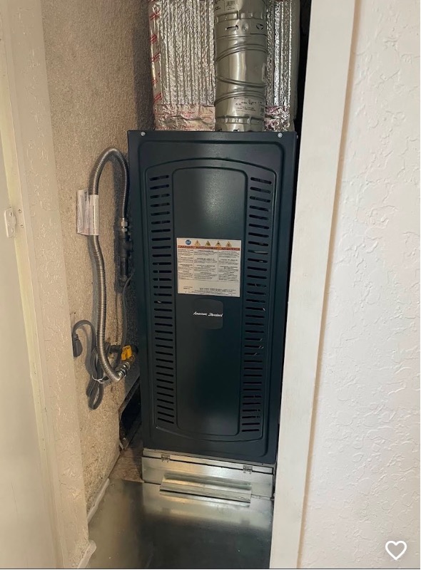 An American Standard furnace installed in a narrow utility closet with ductwork above.