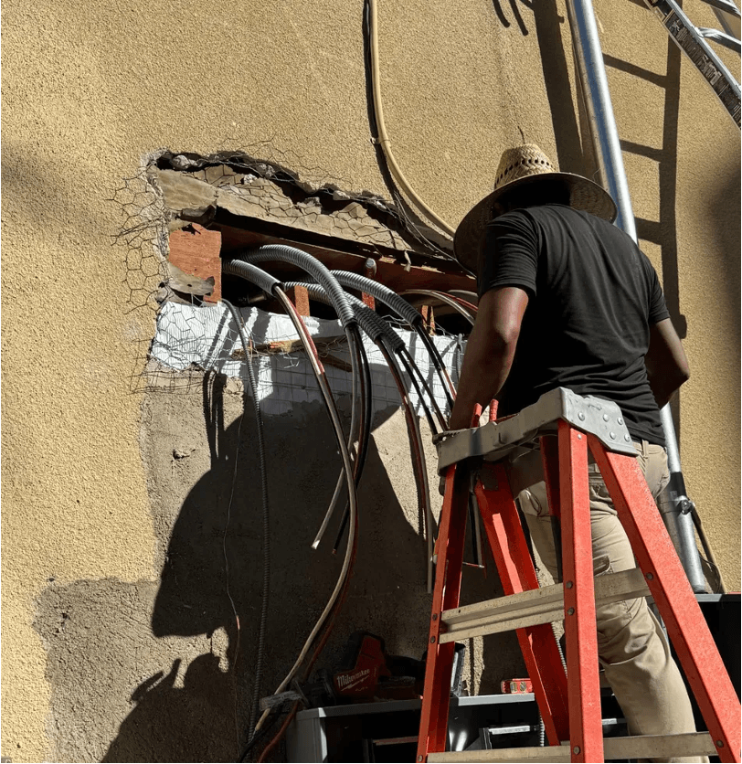 Electrician on a ladder running new wiring through an exterior wall opening
