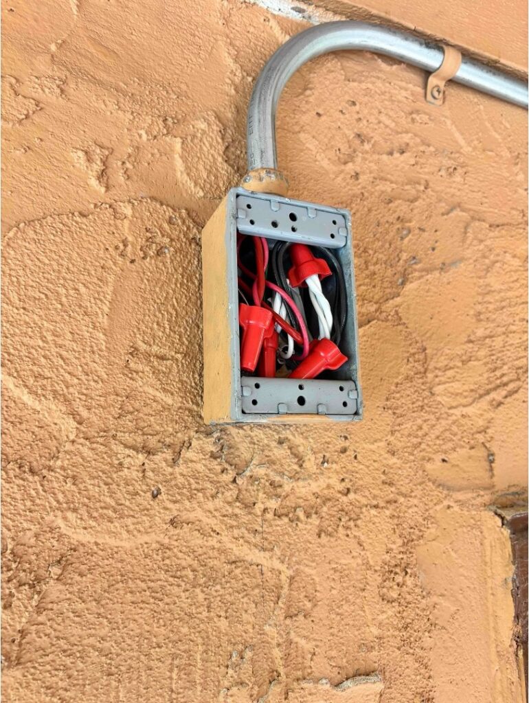 Metal electrical box with wiring and wire nuts, fed by metal conduit on an exterior wall.