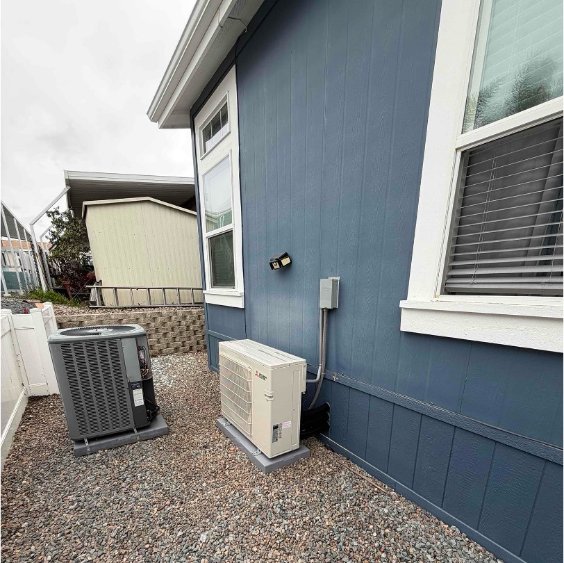 Mitsubishi mini-split outdoor unit and traditional AC condenser beside a blue house exterior.