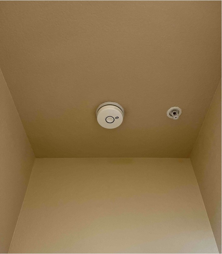 A ceiling-mounted smoke detector next to a fire sprinkler head