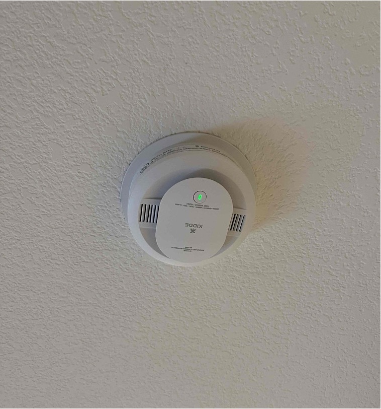 A round white smoke detector mounted on a ceiling with its status indicator light on