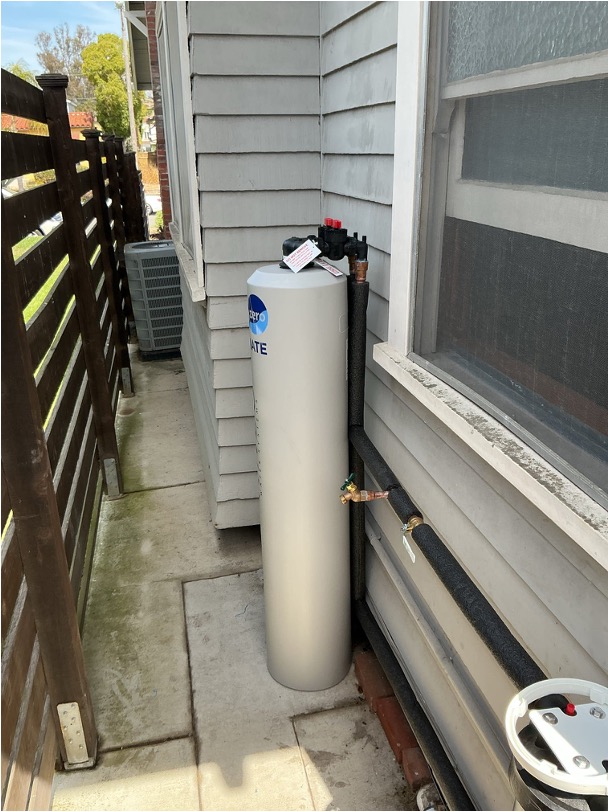 An outdoor whole-house water treatment tank installed along the exterior wall of a home