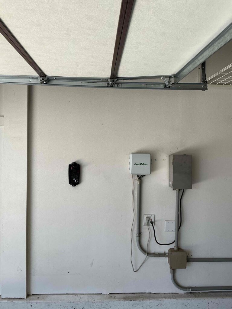 EV charger equipment mounted in a garage with conduit, a disconnect box, and a 240-volt outlet on the wall.