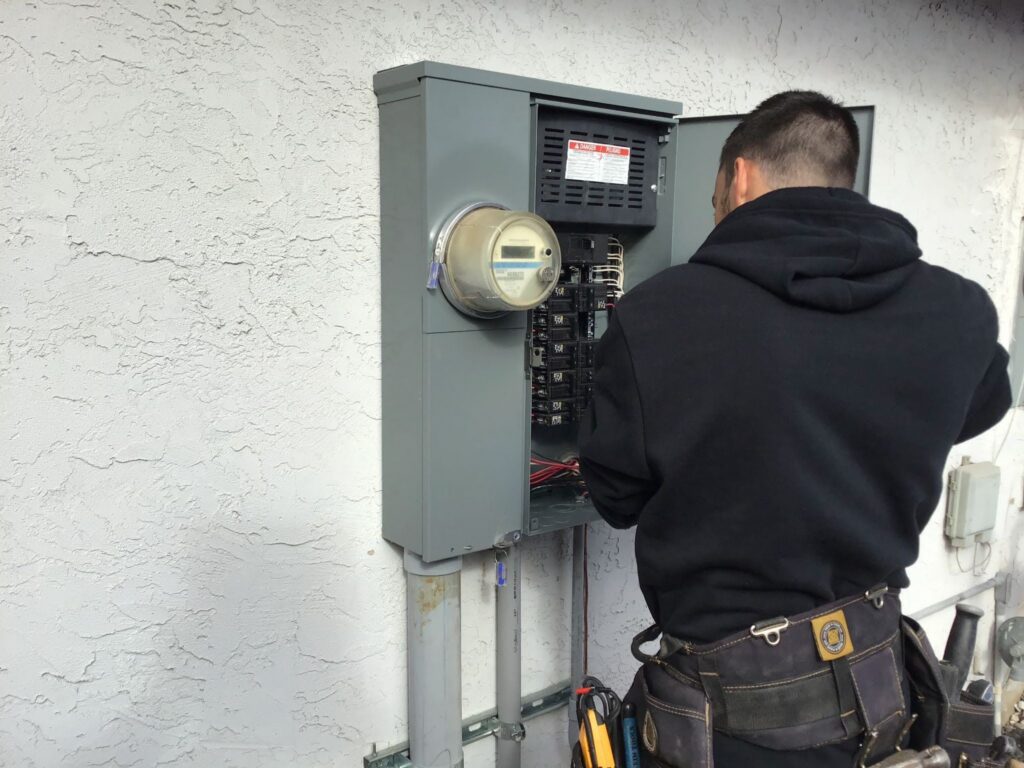 Licensed electrician working at an open residential meter-main panel with a tool belt.