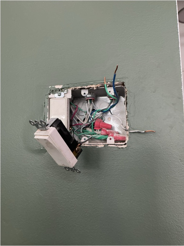 Open electrical box with a light switch pulled out, exposing tangled wires and red wire nuts