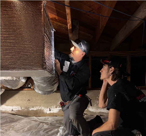 Two Point Loma Home Pros technicians in branded shirts inspecting ductwork and insulation in an attic space.