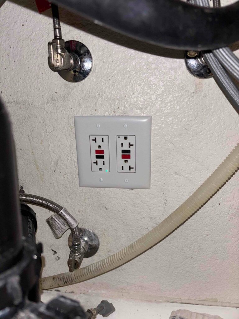 Two white GFCI outlets with test and reset buttons installed on a wall surrounded by plumbing supply lines.