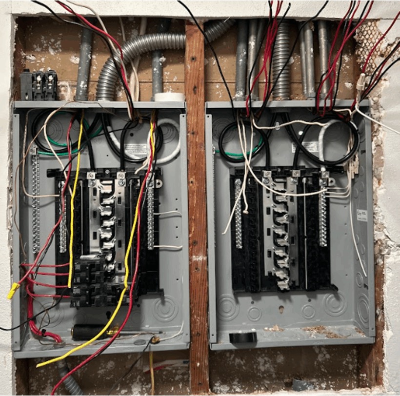 Two open residential electrical panels mounted side by side with exposed wiring and circuit breakers visible